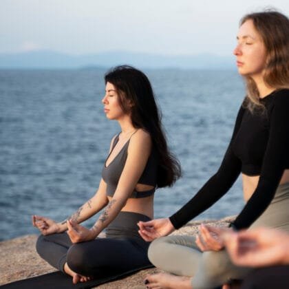 Two women seated on the coast meditating with closed eyes as part of a Mantra Chanting Course