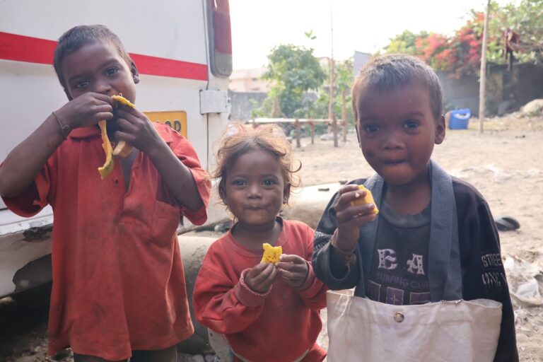 Three homeless children in Rishikesh holding bananas, looking toward the camera