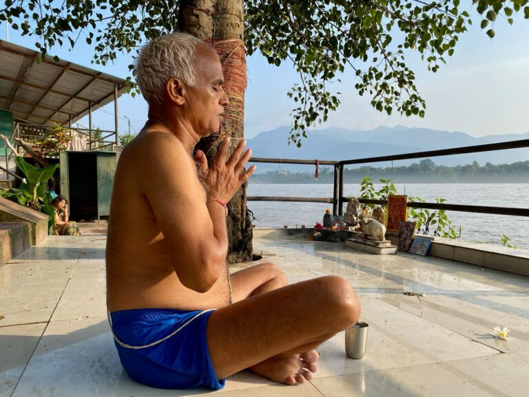 Person meditating in lotus pose by the Ganga River in Rishikesh